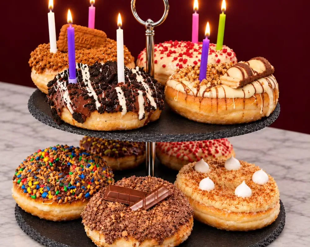 Présentoir à deux étages de donuts gourmands avec bougies d’anniversaire allumées